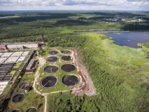 Primary settling tanks and clarifiers are on wastewater treatment plant in evergreen forest. Aerial view