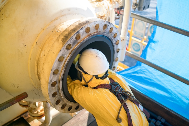 Worker cleaning internal pressure vessel in confine space.